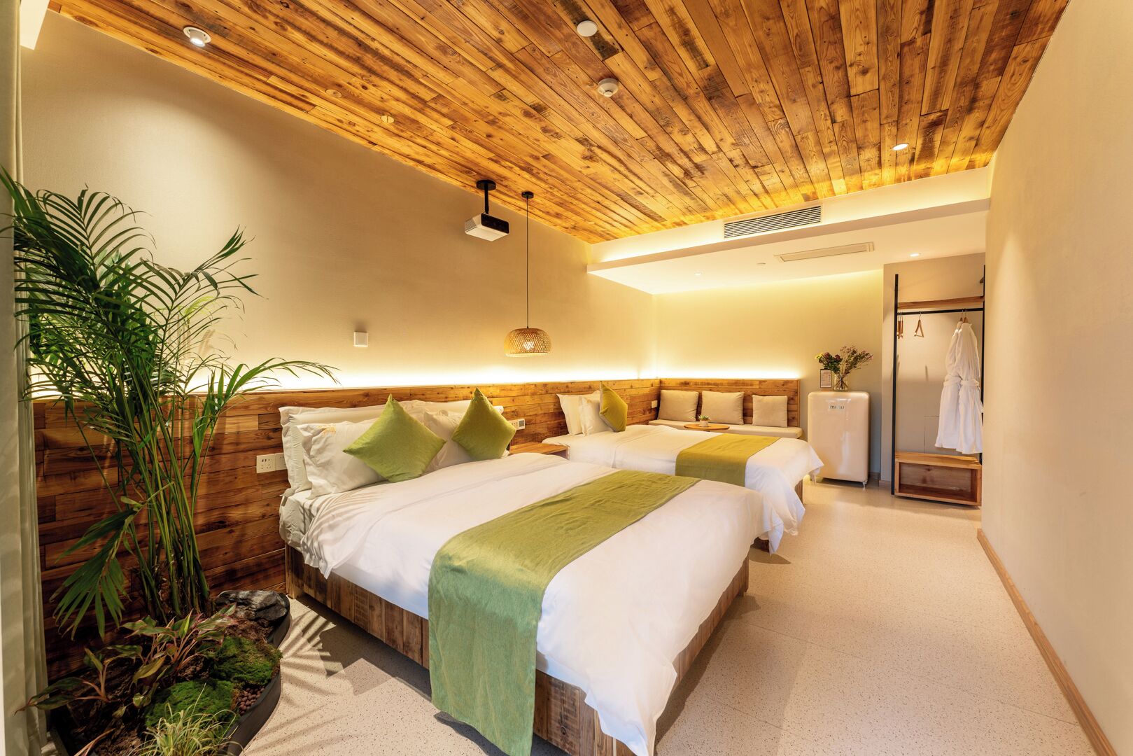 Ein Hotelzimmer mit zwei Betten, Holzboden, einer Pflanze und einem Spiegel.