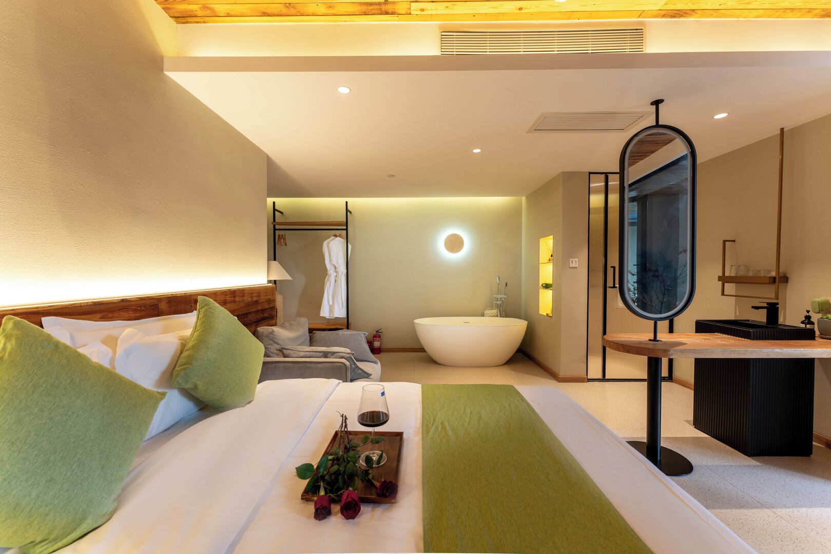 A hotel room with a bed, a large mirror, a bathtub, and a vanity area.