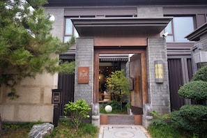 A building entrance with a stone facade, a wooden door, and a small garden area with a spherical object. - Luming Courtyard Hotel Xi'an City Wall (Xi'an)