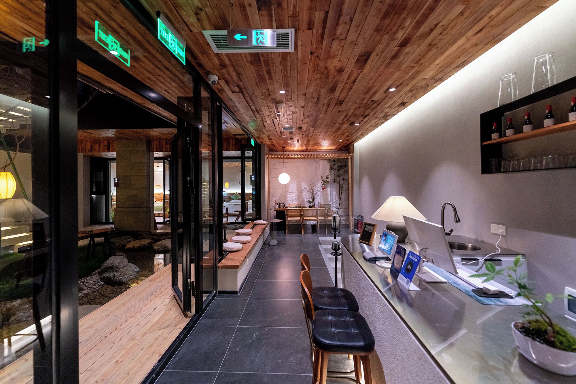 A modern interior with a wooden ceiling, a reception desk, seating area, and a visible outdoor view.