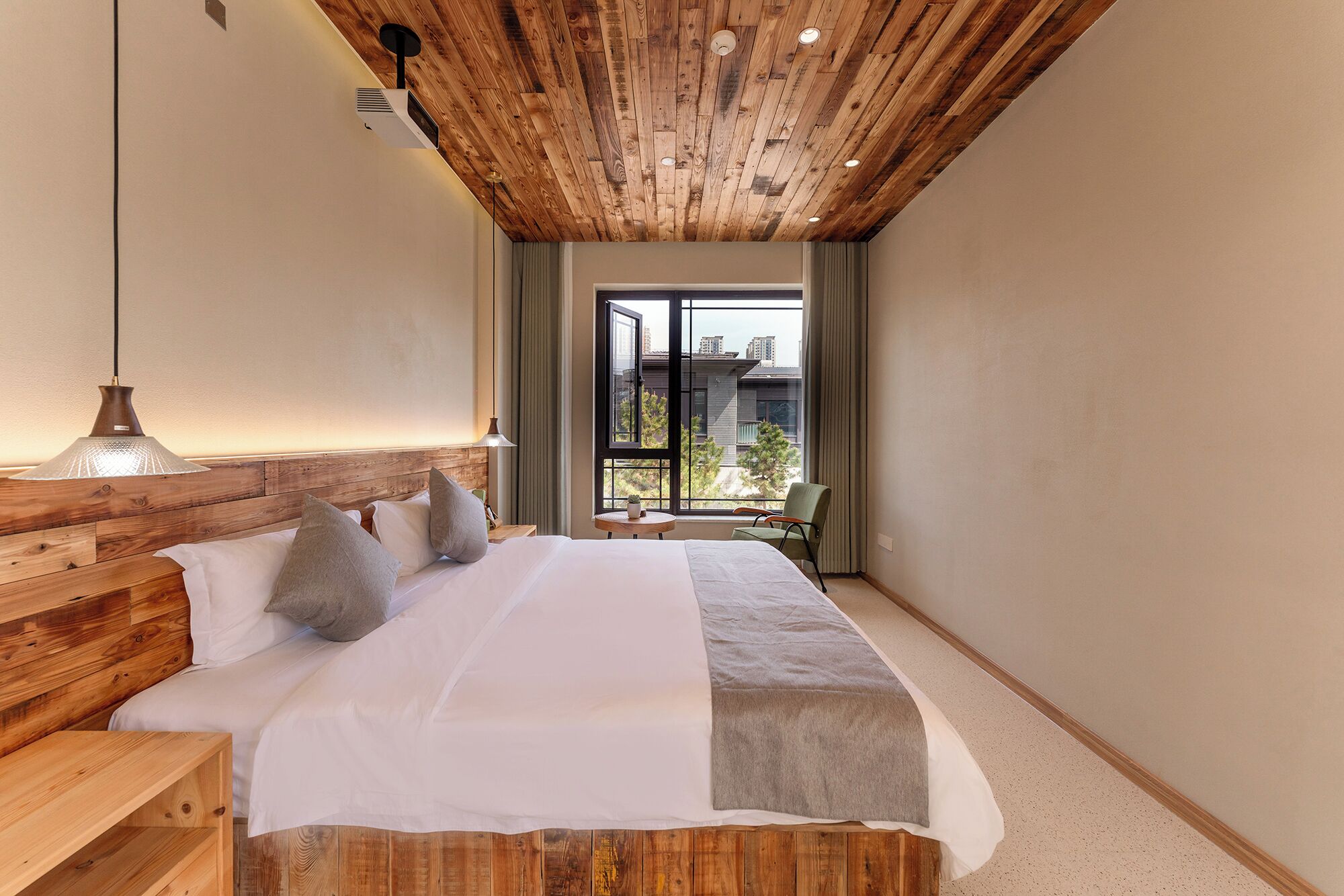 Une chambre avec un plafond en bois, un grand lit avec une literie blanche, une table de chevet, une lampe et une vue sur l’extérieur.