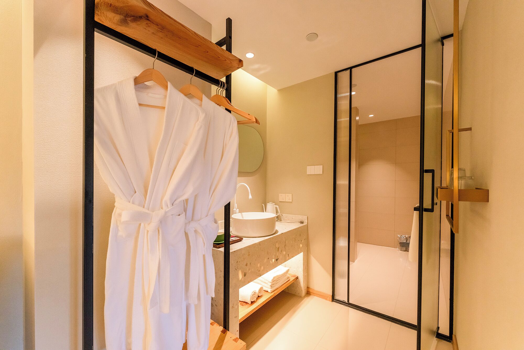 Un baño moderno con cabina de ducha de vidrio, una bata blanca colgada en un perchero y un tocador con espejo.