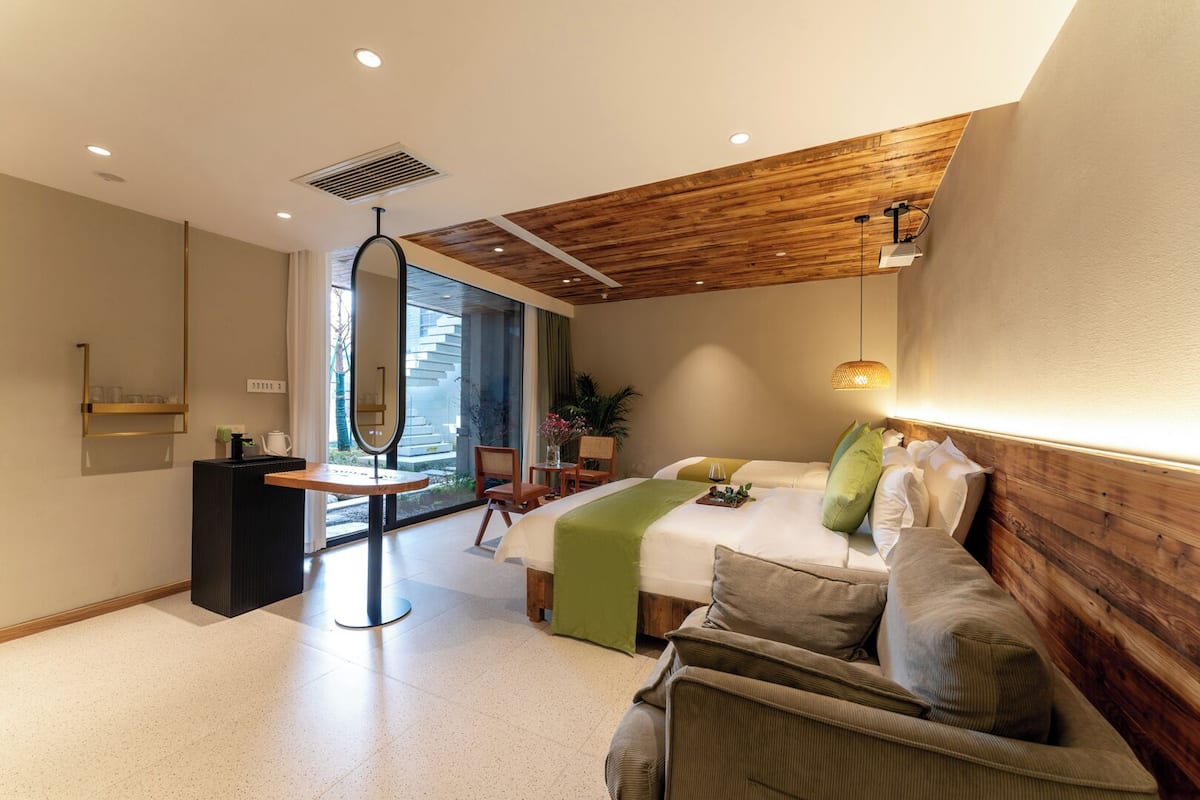 A modern hotel room with a bed, seating area, and a view through a glass door.