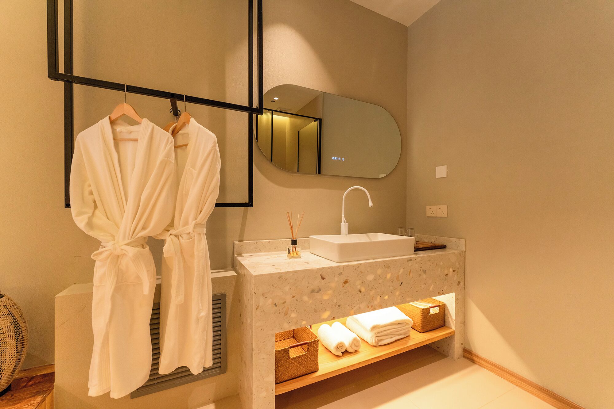 A bathroom with a sink, mirror, robe hanging, and a shelf with towels.