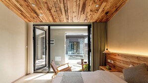 Ein Hotelzimmer mit Holzbalkendecke, einem Bett, einem Stuhl, einem Tisch und Blick ins Freie.