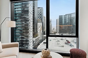 Ein modernes Hotelzimmer mit großem Fenster, das Blick auf Hochhäuser und einen Parkplatz bietet.