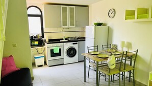 Une cuisine compacte équipée d’un lave-linge, d’un four et d’un four à micro-ondes. Elle comprend également un coin repas avec une table dressée pour deux personnes.