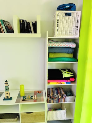 Ein ordentlich eingerichteter Raum mit Regalen, auf denen Bücher, ein kleines Spielzeugleuchtturm und ein Korb stehen.