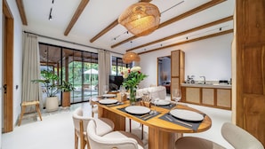A modern dining area with a wooden table set for six, surrounded by chairs, and a large window offering a view of greenery. - Villa Sorento (Petulu)