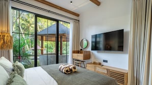 A bedroom with a large bed, a TV, a wooden desk, and a view of greenery outside. - Villa Sorento (Petulu)