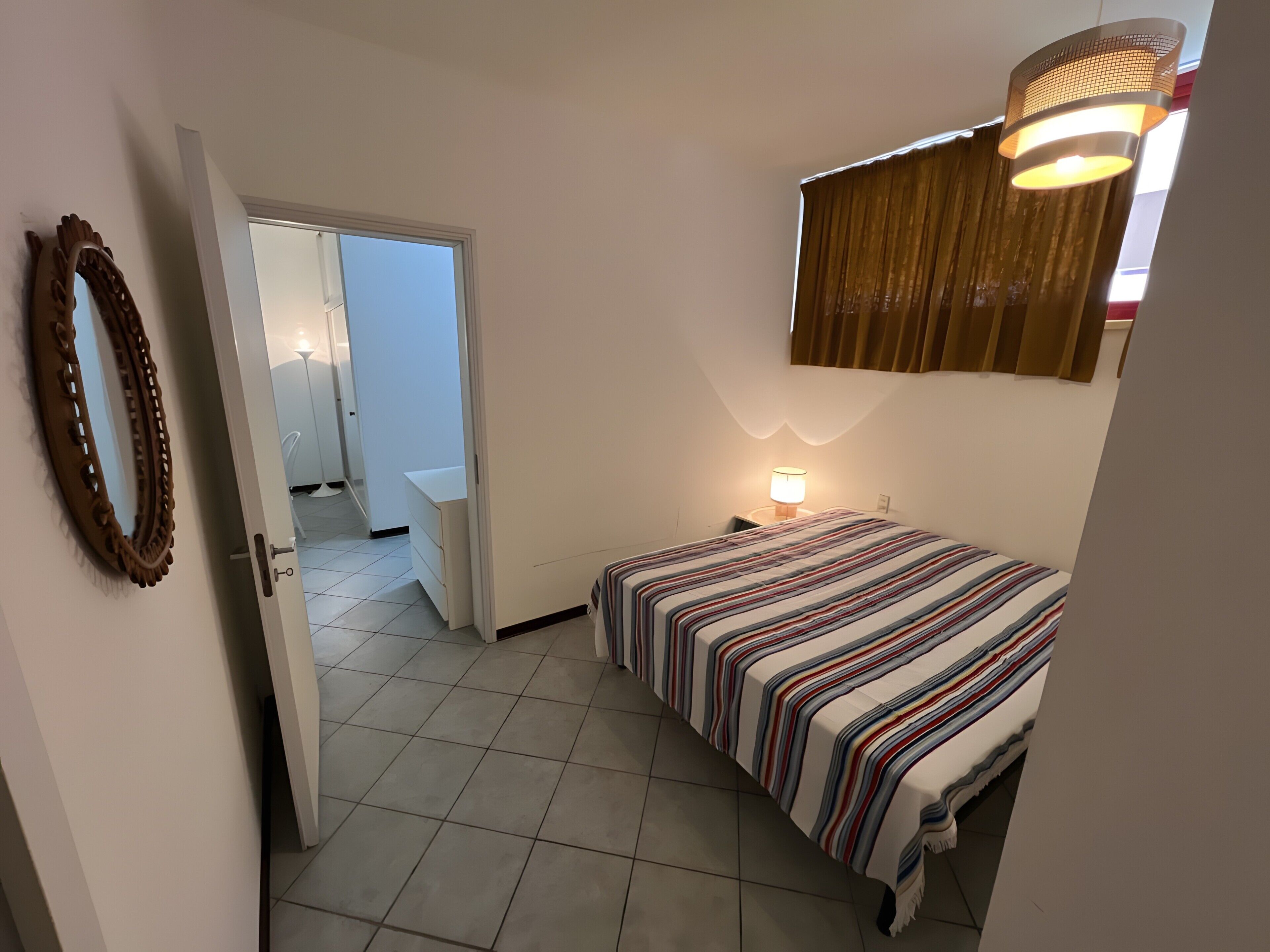 A bedroom with a bed, a bedside lamp, a mirror, and a door leading to a bathroom.