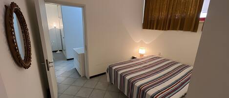 A bedroom with a bed, a bedside lamp, a mirror, and a door leading to a bathroom.