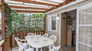 Un espacio al aire libre cubierto con una mesa y sillas, una terraza de madera, una puerta con la inscripción 'Bain' y una ventana con vistas a la vegetación.