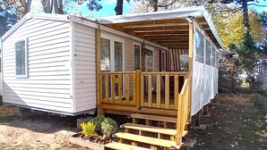 Una pequeña casa móvil de un solo piso con terraza de madera y porche delantero.