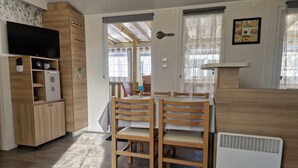 Una habitación con una mesa de madera, sillas, un televisor y una kitchenette.