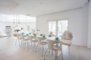A modern dining area with white furniture, a large sculpture, and a view through a glass door.