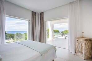A bedroom with a large bed, a view of the outdoors, and a balcony with a table and chairs.