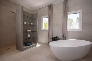 A modern bathroom with a freestanding bathtub, a glass shower enclosure, and a window providing natural light.