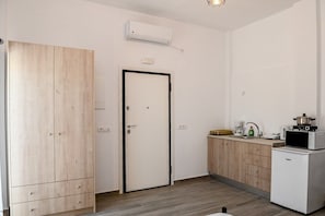 Ein kleiner, moderner Raum mit einem Holzschrank, einer weißen Tür, einer Küchenzeile mit einer Mikrowelle und einer eingebauten Klimaanlage.