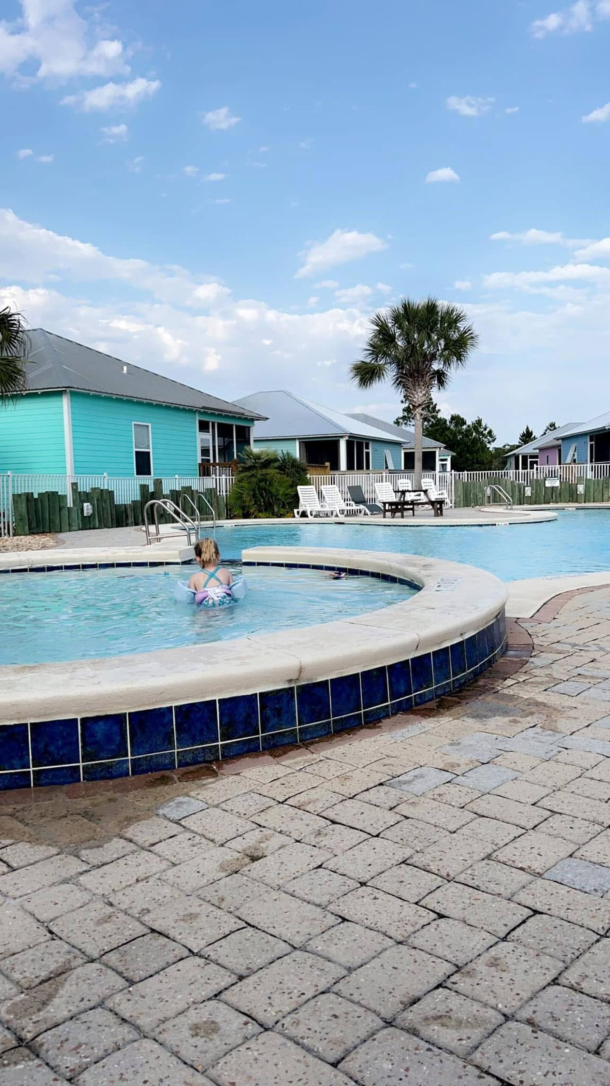 A swimming pool with a tiled edge, a child in the water, and a palm tree.