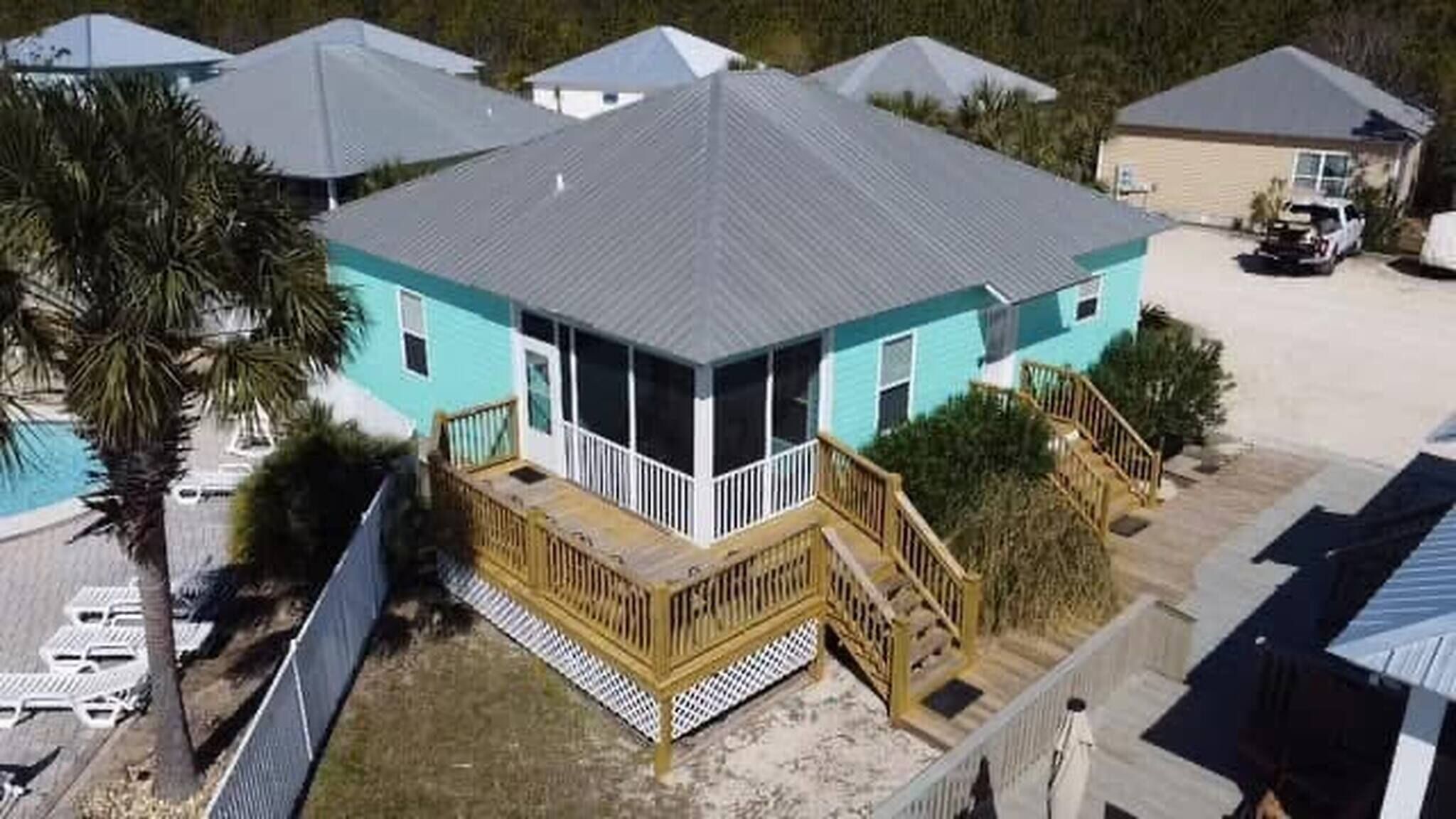 A turquoise house with a screened porch, a wooden deck, and a fenced yard.