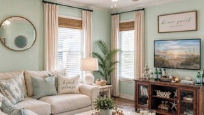 Ett vardagsrum med en beige soffa, ett soffbord med snacks, en tv och en bokhylla.