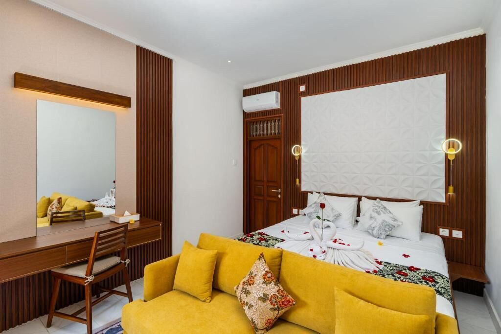 A hotel room with a bed, a wooden desk, a yellow sofa, and a large mirror.