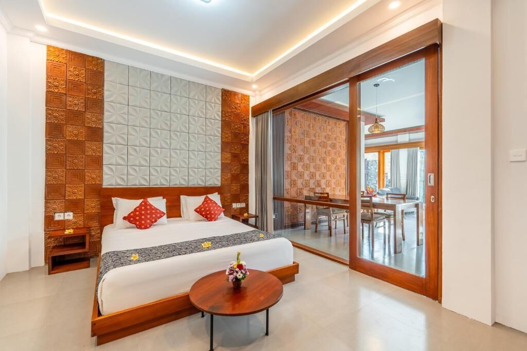 A hotel room with a large bed, a small table with a vase, a sliding glass door to a balcony, and a patterned wall.