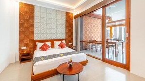Habitación de hotel con cama, una mesa redonda de madera, un balcón con zona de comedor y una puerta corrediza de vidrio.