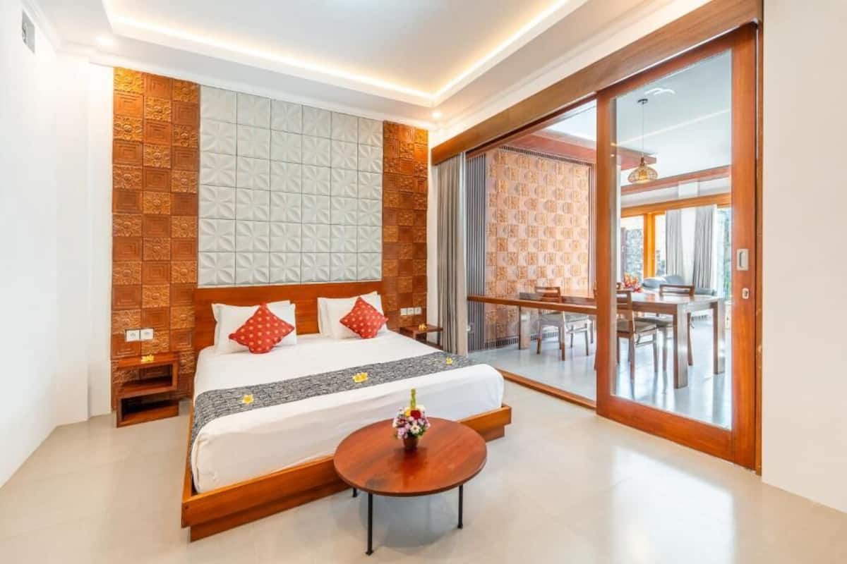 A hotel room with a bed, a round wooden table, a balcony with a dining area, and a sliding glass door.