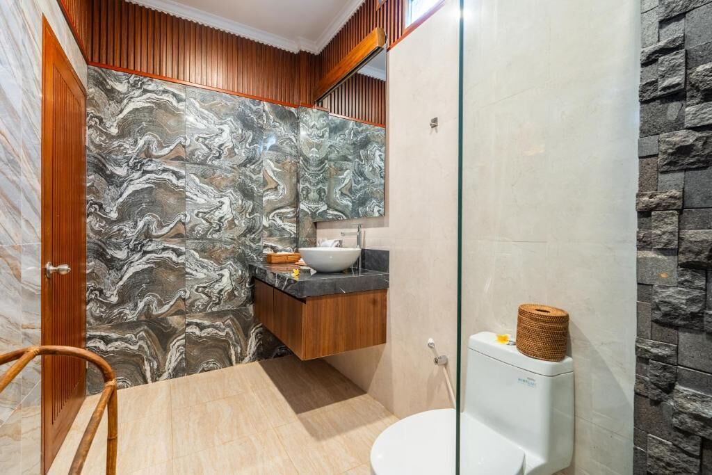 A bathroom with a marble backsplash, wooden vanity, and a glass shower enclosure.