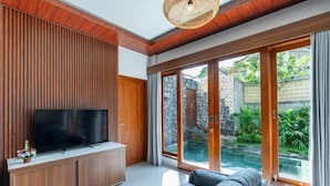 Una sala de estar moderna con una televisión de pantalla plana, paneles de madera, un sofá y puertas correderas de cristal que dan a una zona de piscina.