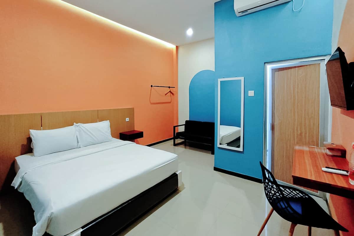 A hotel room with a bed, a desk, a chair, a mirror, and an air conditioning unit.