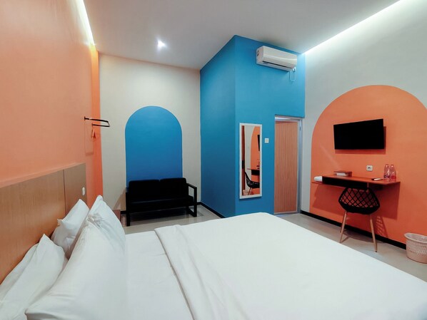 Quarto de hotel com cama, escrivaninha, cadeira, ar condicionado e televisão.