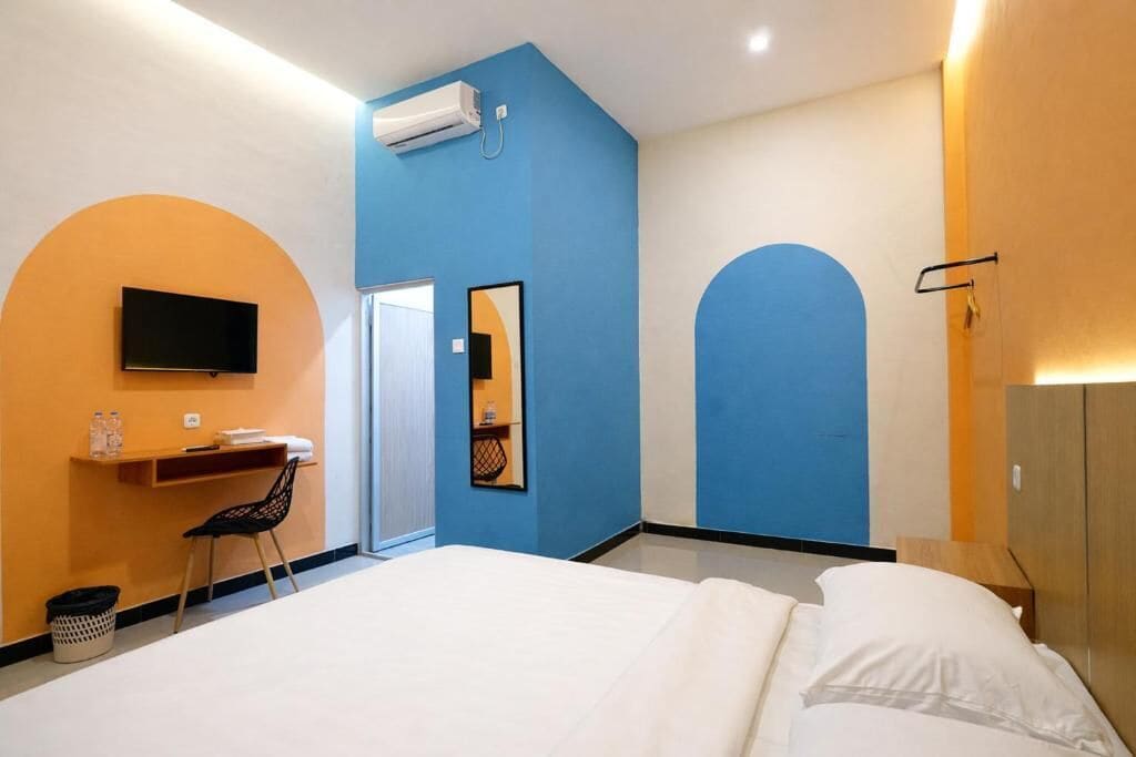 Ein Hotelzimmer mit Bett, Schreibtisch mit Stuhl, Fernseher, Spiegel und Klimaanlage.