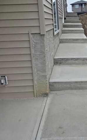 A residential building with beige siding, a stone foundation, and concrete steps leading to the entrance. - Cozy Irvine Creek Walk-Out Suite 10 mins to YEG (Leduc County)