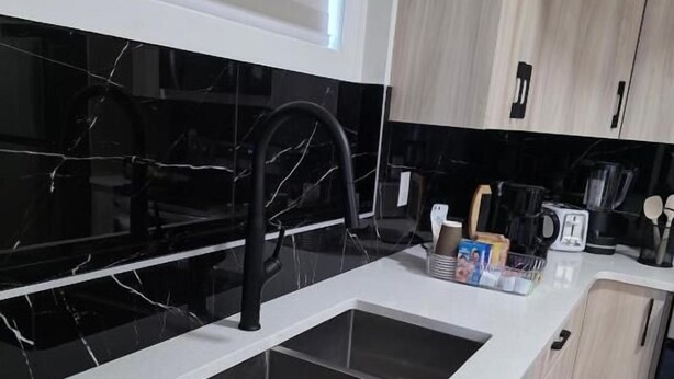 Moderni keittiö, jossa on musta marmoripintainen välitila, valkoinen työtaso ja musta hana. Työtasolla on ruukkukasvi ja oikealla kahvinkeitin.