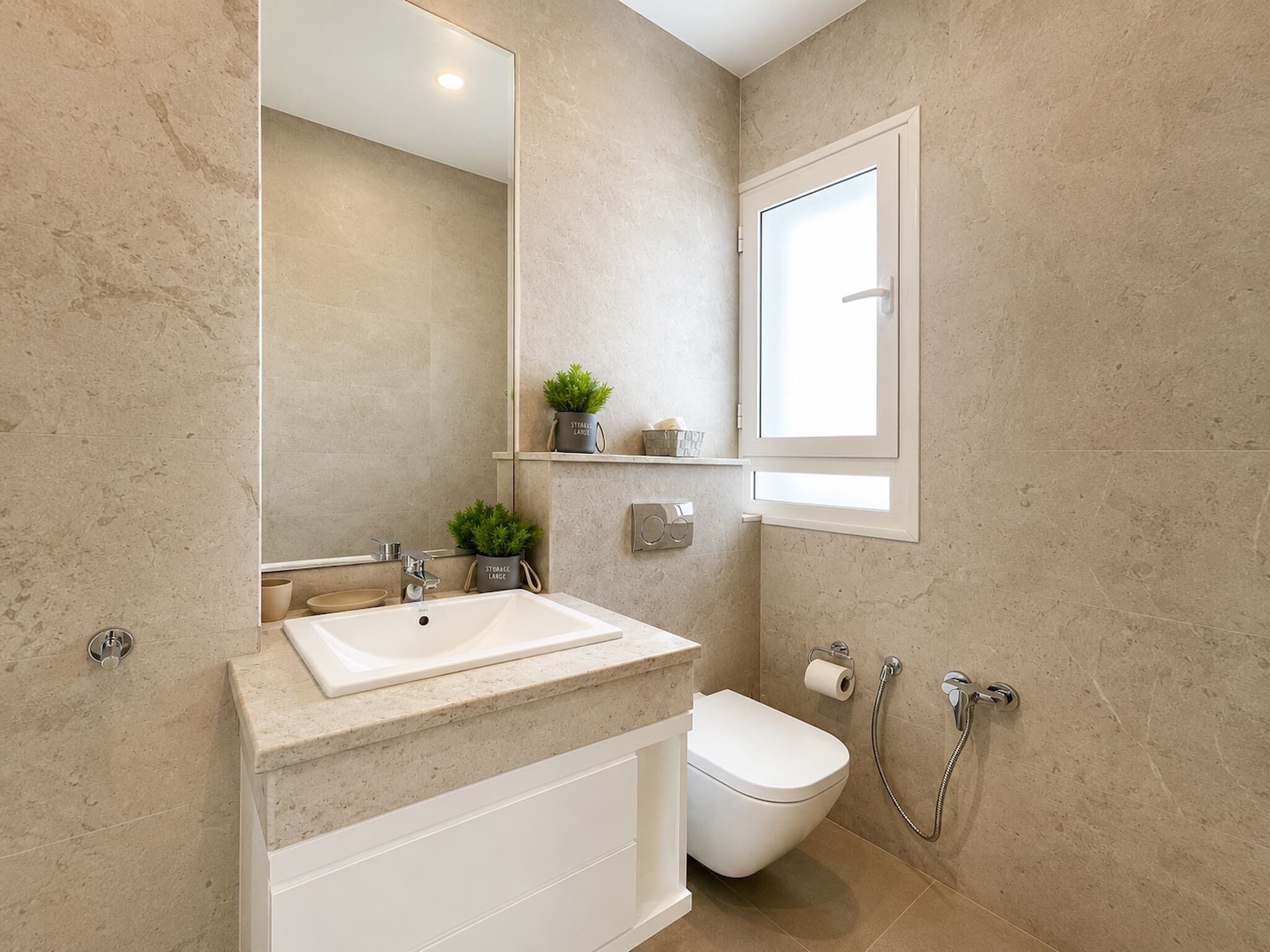 A bathroom with a white sink, toilet, and shower. There is a mirror, a shelf with a plant, and a window.