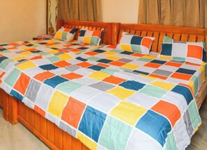 Een tweepersoonsbed met een kleurrijke sprei, een houten hoofdbord en gordijnen.