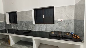 Una cocina con encimera negra, dos ventanas, una estufa a gas y un lavabo.