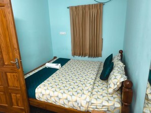 A room with a bed, a wooden door, a window with curtains, and a wall socket. - Miraya Resort (Kuilapalayam)