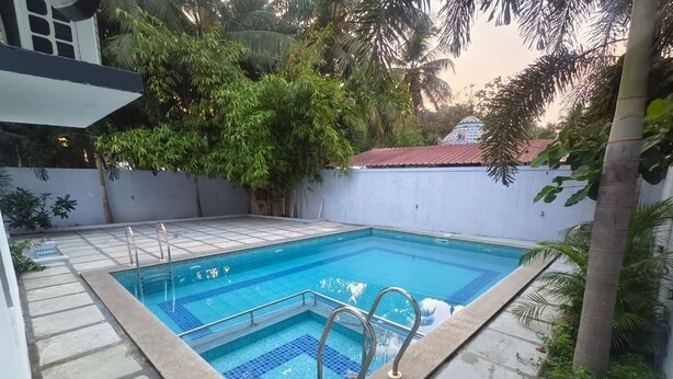 Una piscina rectangular con borde de baldosas y barandas metálicas, rodeada por un muro bajo y abundante vegetación.
