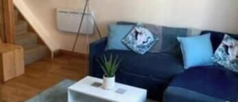 A living room with a sofa, a coffee table, a plant, a painting, and a staircase.