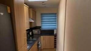 A narrow kitchen with wooden cabinets, a black refrigerator, and a microwave. - Stratos Realty (Newquay)