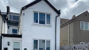 A two-story white house with a front door, windows, and a small front yard with potted plants. - Stratos Realty (Newquay)
