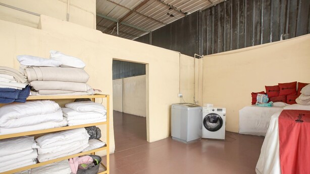 A laundry room with shelves of folded towels, a washing machine, and a bed with a red headboard. - Luxury Deluxe DBL Retreat W/ Free Wifi and Parking (Batam)