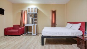 A hotel room with a bed, a red chair, a small table with a bottle, and a TV mounted on the wall. - Luxury Deluxe DBL Retreat W/ Free Wifi and Parking (Batam)