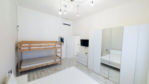 Quarto com cama de solteiro e beliche, guarda-roupa, televisão e luminária de teto.