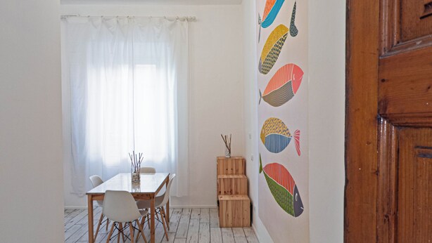 Quarto com piso de madeira, uma mesa de jantar com cadeiras, um lustre no teto e uma parede com desenhos de peixes coloridos.