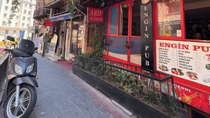 Vista da rua com um prédio exibindo uma placa com os dizeres 'ARIF MUZIKHOL' e 'ENGIN PUB'.